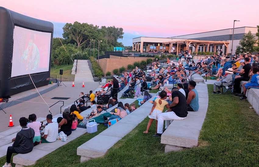 Families enjoying outdoor movie night at the Champlin Riverside amphitheater at sunset