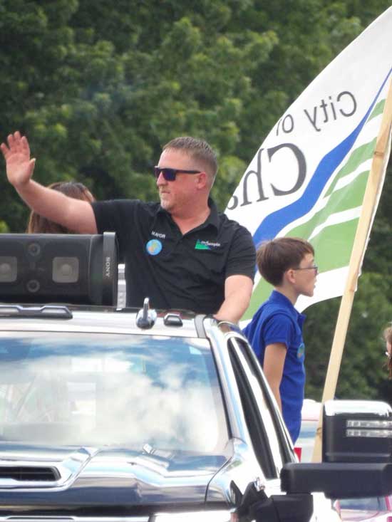 Mayor Ryan Sabas waving from a parade float with the City of Champlin flag